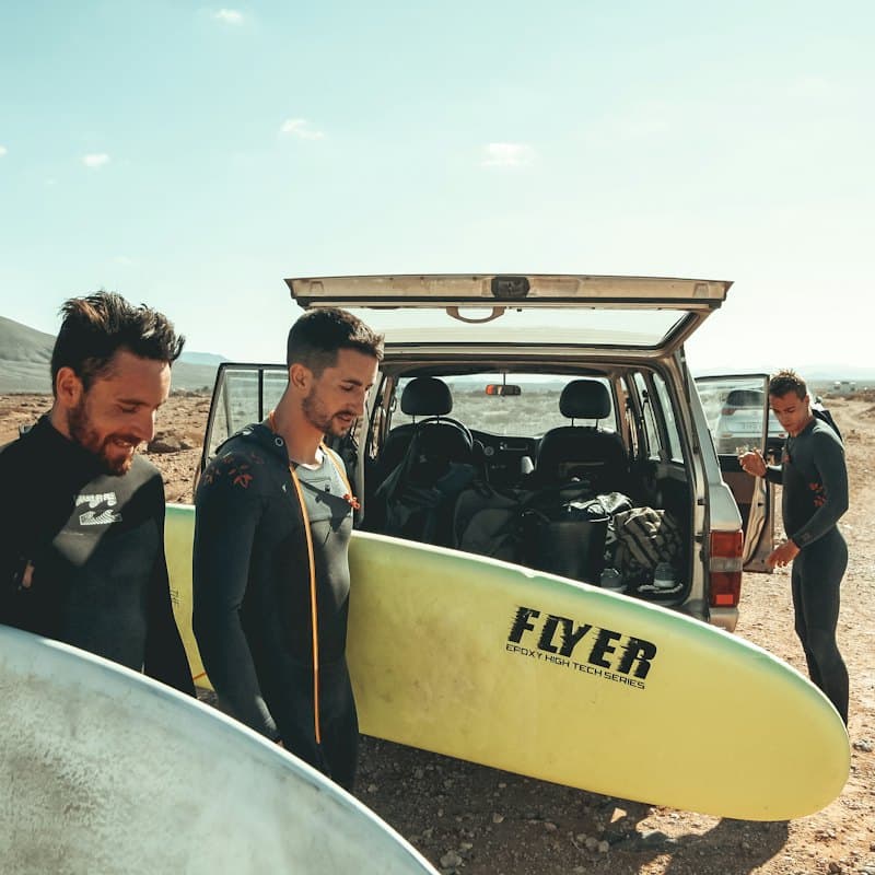 Friends in wetsuits with a surfboard by their van