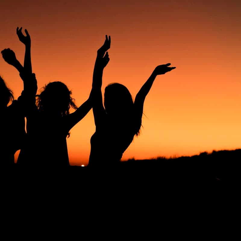 Three women dancing with their arms up at sunset