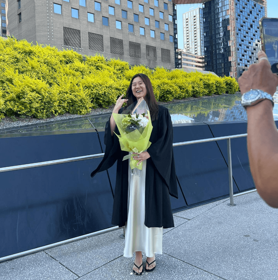 A graduate holding flowers, laughing, as someone takes her photo