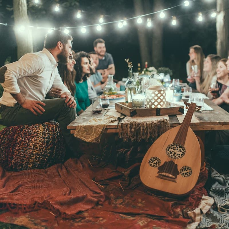 Friends at an outdoor dinner on blankets, one playing an oud