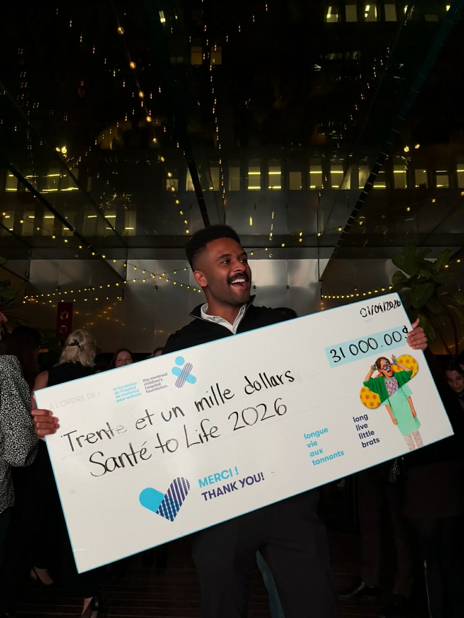 Holding a giant Santé 2 Life cheque