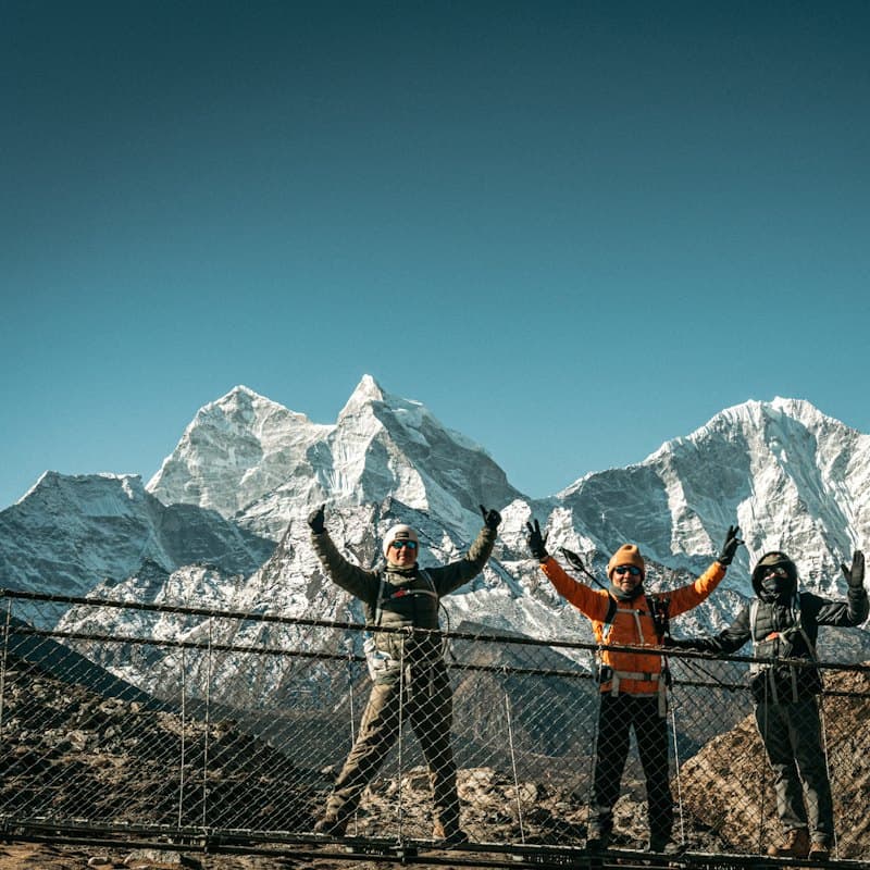 Three hikers cheering on a suspension bridge in the mountains